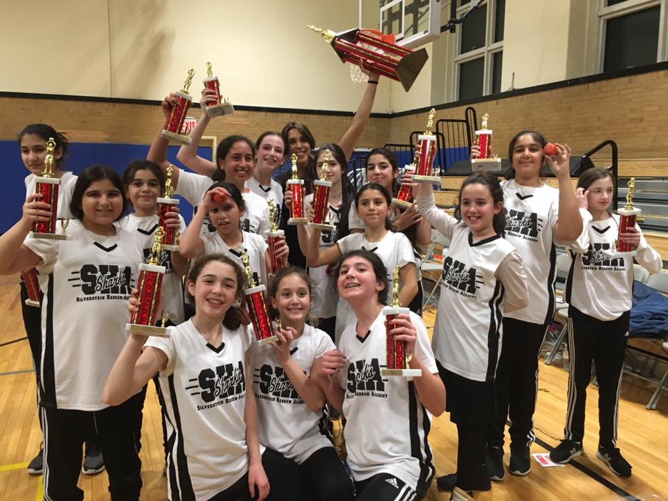 Members of Silverstein Hebrew Academy's Girls Basketball Lady Sharks team hold their championship trophies on the court, celebrating an undefeated season and championship victory. (Photo courtesy of Silverstein Hebrew Academy)