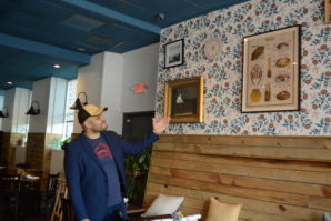 Villalona gestures to works on the wall of Element Seafood, some of which he said are heirlooms of Nellie Wu's family, which initially helped start the venture. (Photo by Janelle Clausen)