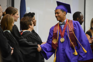 A student garbed in honors goes to shake hands with administrators as he collects his high school diploma. (Photo by Janelle Clausen)