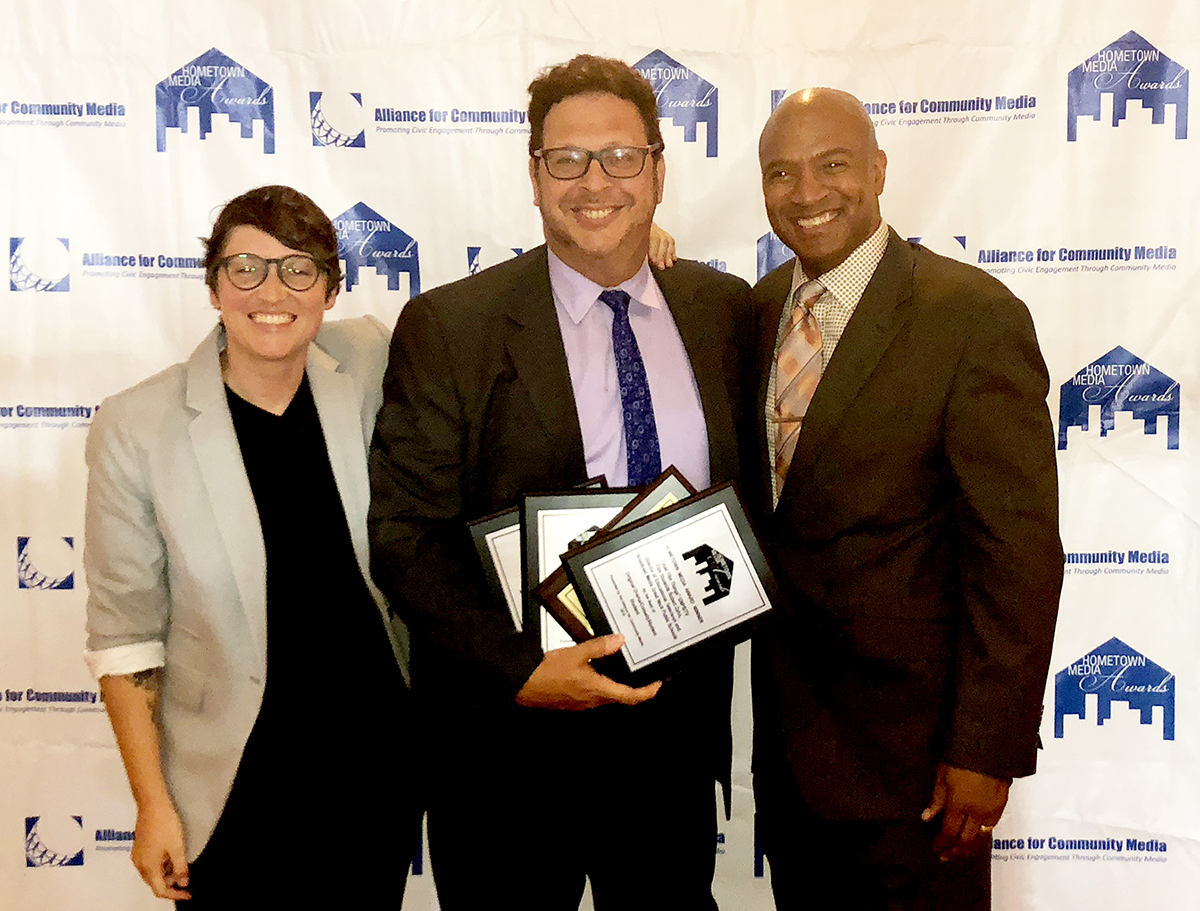 Robert Zahn, educational TV and broadcast media director for the Great Neck Public Schools, is congratulated by Erica Jones and Ulysses E. Campbell, hosts of the 2018 Hometown Media Awards. Mr. Zahn accepted four awards on behalf of GNPS/TV. (Photo courtesy of the Great Neck Public Schools)