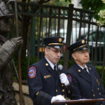 A statue of Jonathan L. Ielpi, a New York City firefighter from Great Neck, looms over Vigilant Fire Chief Joshua Charry as he addresses attendees, with his father Rabbi Marim Charry by his side. (Photo by Janelle Clausen)