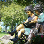 Two bronze children sit perched on a bench underneath a magnolia tree and adjacent to a memorial plaque for Ruth Tamarin. (Photo by Janelle Clausen)