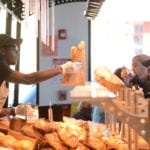 An employee of Marie Blachére passes along a baguette to one of the many customers on line ordering French pastries. (Photo by Janelle Clausen)
