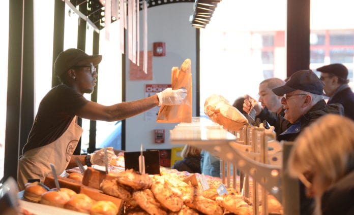 DSC_0328 An employee of Marie Blachére passes along a baguette to one of the many customers on line ordering French pastries. (Photo by Janelle Clausen)