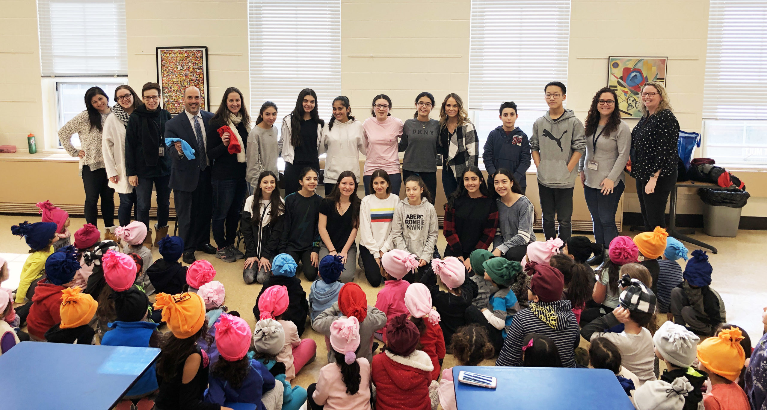 Eighth-graders from the North Middle School FACS program visited the John F. Kennedy School to deliver fleece hats and share a story with kindergarten students. Lauren Neckin, department chair for FACS, and her North Middle students are photographed with Kennedy School faculty Alyssa Gies, special education teacher; Christina Russo, kindergarten teaching assistant; Judy Friedman, kindergarten teacher; Ron Gimondo, principal; Michelle Reiter, kindergarten teacher; Gabby Kishinevsky, kindergarten teacher; and Michelle Bell, assistant principal. (Photo courtesy of the Great Neck Public Schools)